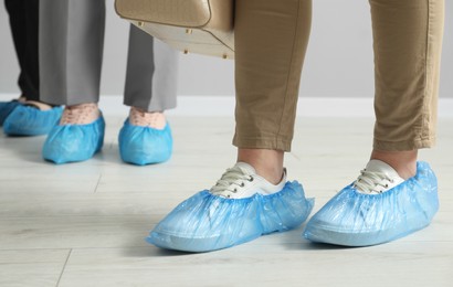 Photo of Women wearing blue shoe covers onto different footwear indoors, closeup