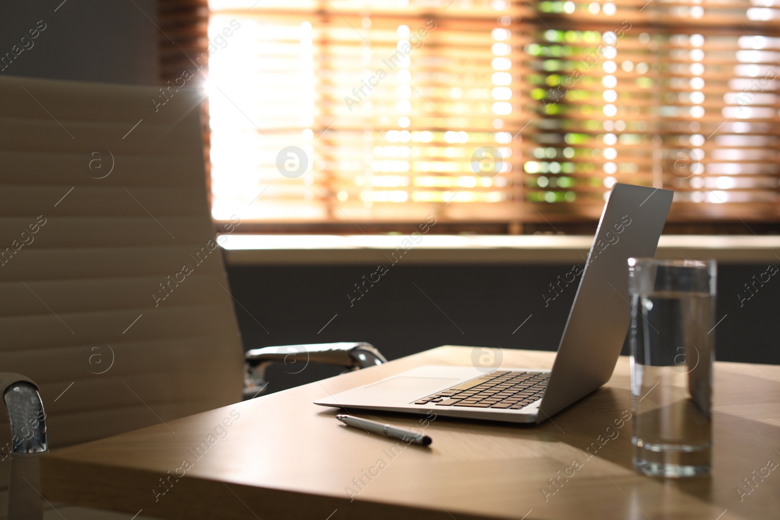 Photo of Laptop and glass of water on wooden table in modern office