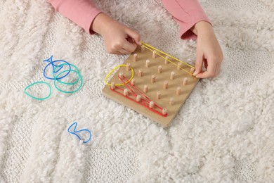 Photo of Motor skills development. Girl playing with geoboard and rubber bands on carpet, closeup