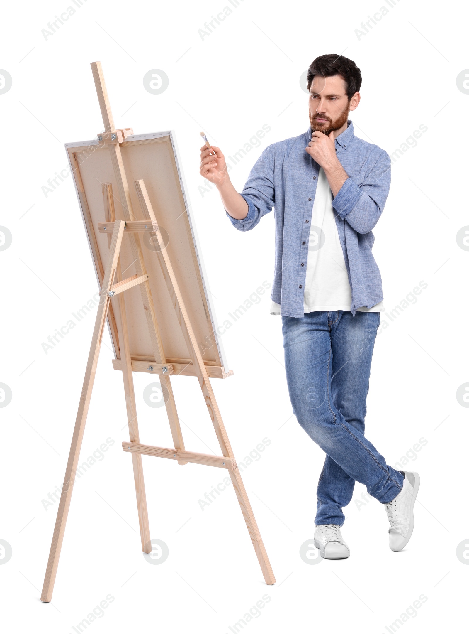 Photo of Man painting with brush against white background. Using easel to hold canvas