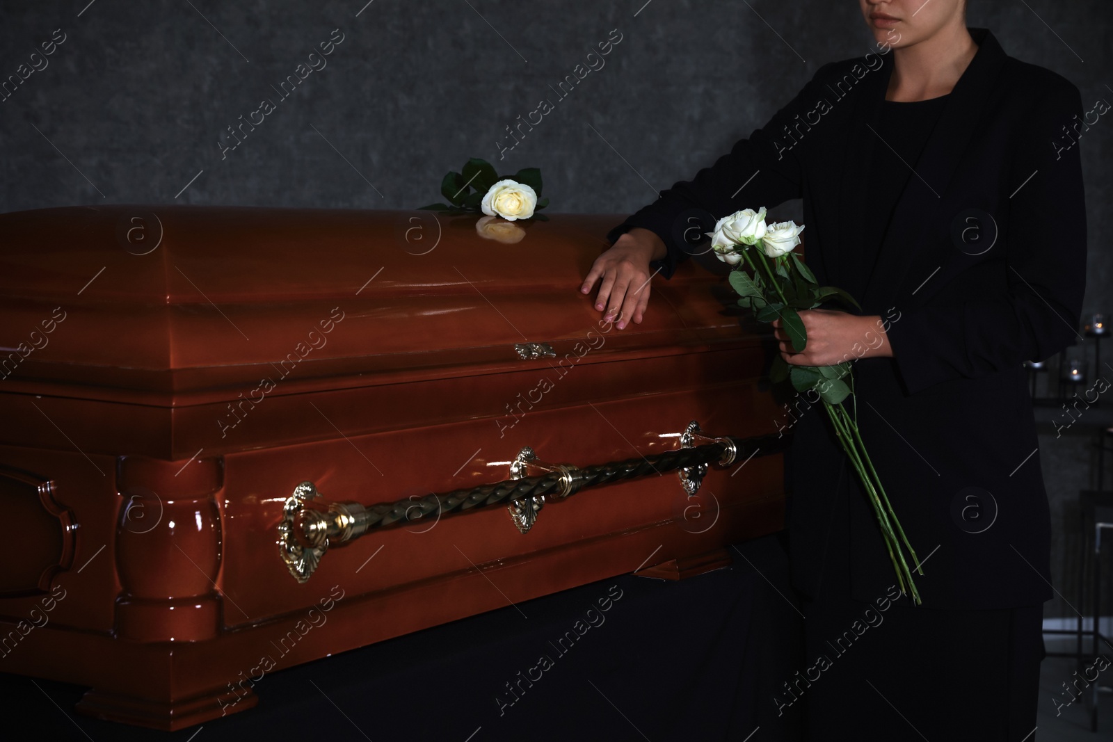 Photo of Young woman with white roses near casket in funeral home, closeup