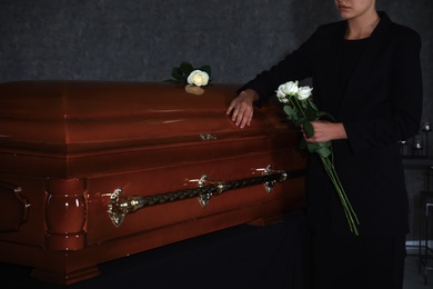 Young woman with white roses near casket in funeral home, closeup