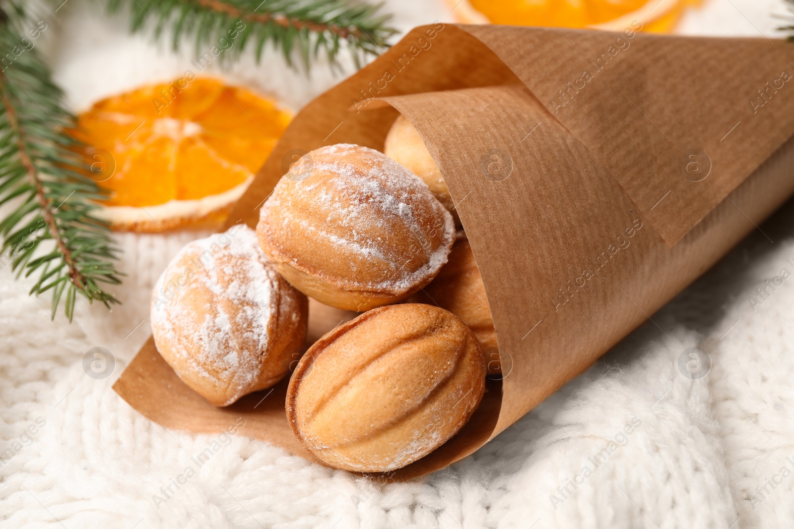 Photo of Delicious nut shaped cookies, dried orange slices and fir tree branches on white knitted fabric, closeup