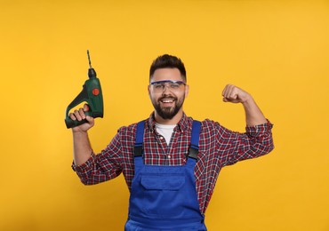 Young worker in uniform with power drill on yellow background