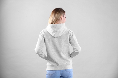 Woman in hoodie sweater on light background. Space for design