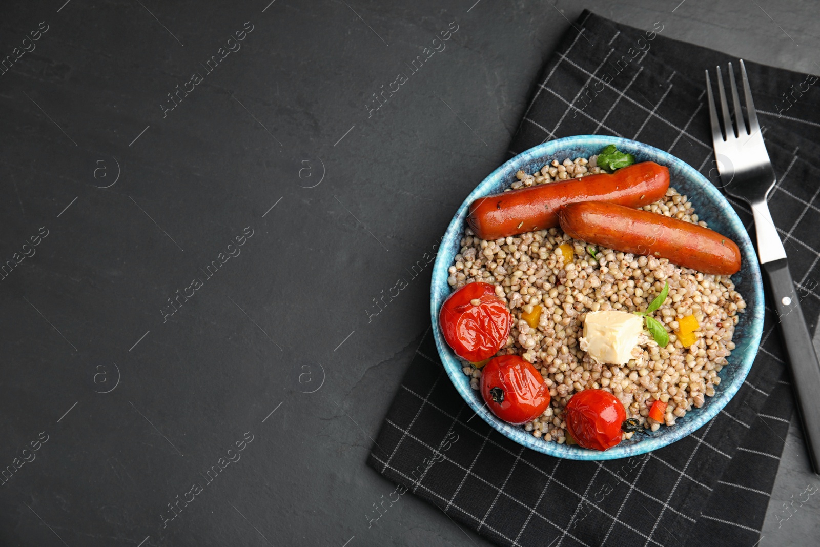 Photo of Tasty buckwheat porridge with sausages on dark grey table, flat lay. Space for text