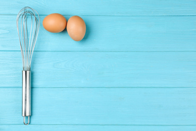Photo of Raw eggs and whisk on light blue wooden table, top view with space for text. Baking pie
