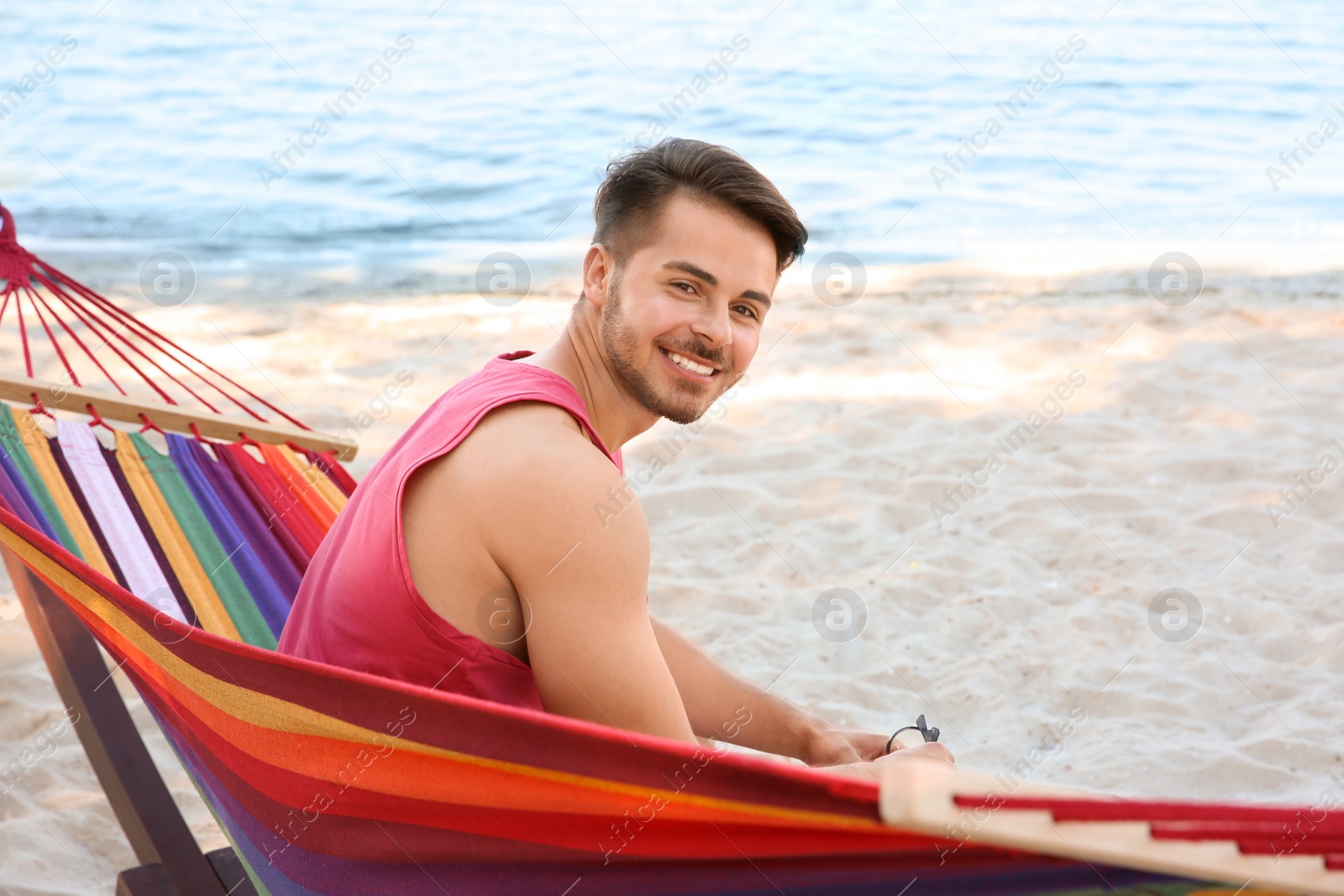 Photo of Young man sitting in colorful hammock at seaside