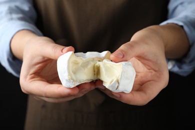 Photo of Woman breaking delicious brie cheese on black background, closeup