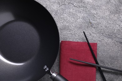 Empty iron wok and chopsticks on grey table, flat lay