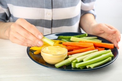 Photo of Woman dipping celery stick in sauce at white wooden table, closeup