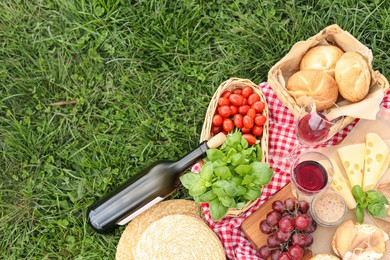 Photo of Picnic blanket with wine and food on green grass, top view