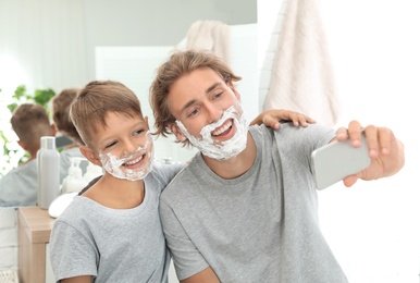 Photo of Father and son taking selfie with shaving foam on faces in bathroom