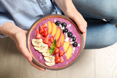 Woman holding bowl with tasty acai smoothie and fruits, top view