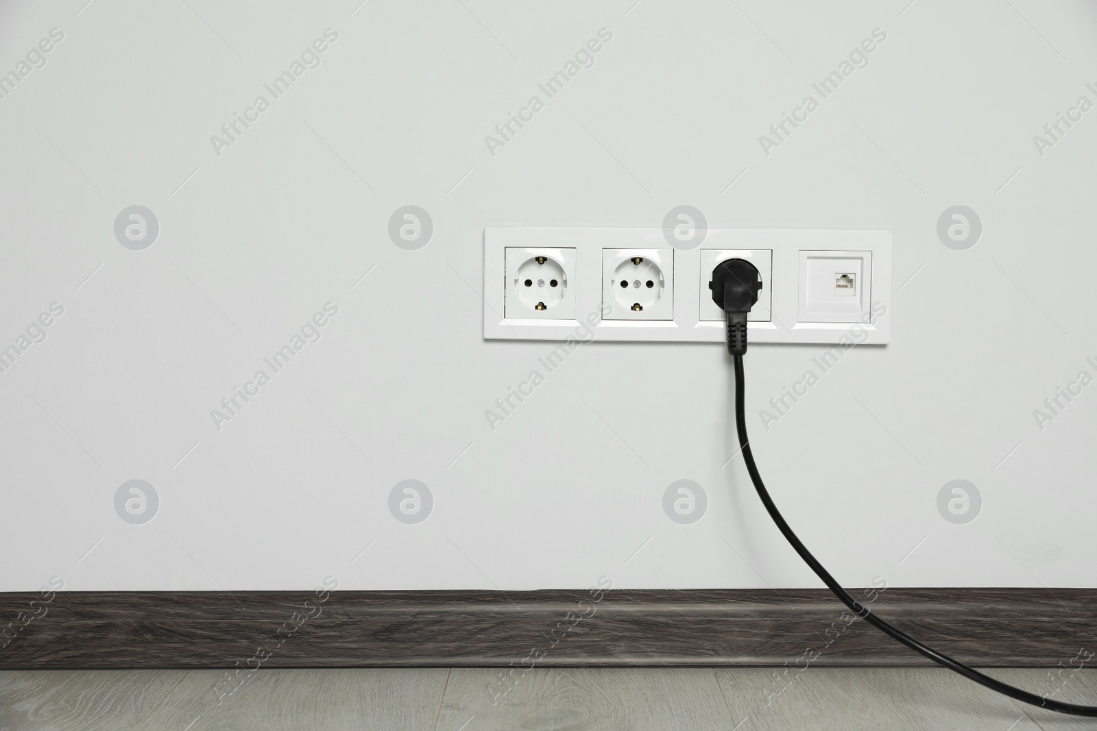 Photo of Power sockets with inserted plug on white wall indoors, space for text. Electrical supply