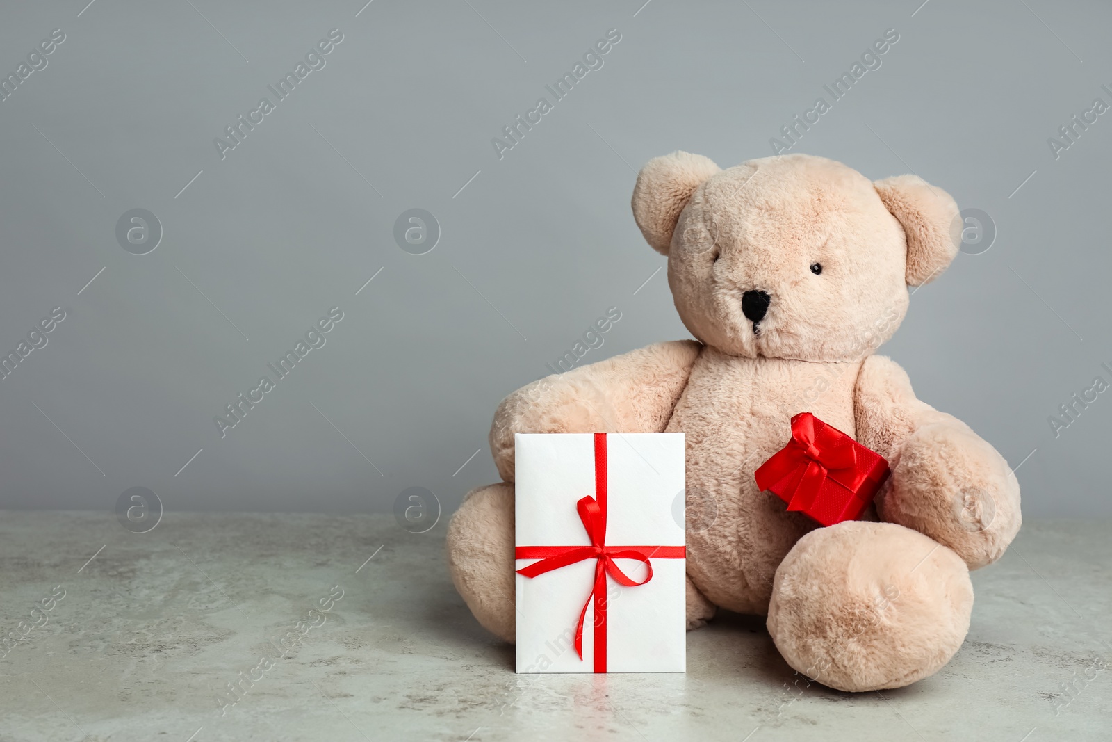 Photo of Cute teddy bear with gift box and envelope on light grey table, space for text. Valentine's day celebration
