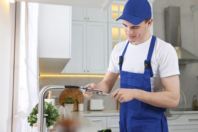 Photo of Young plumber repairing faucet with spanner in kitchen