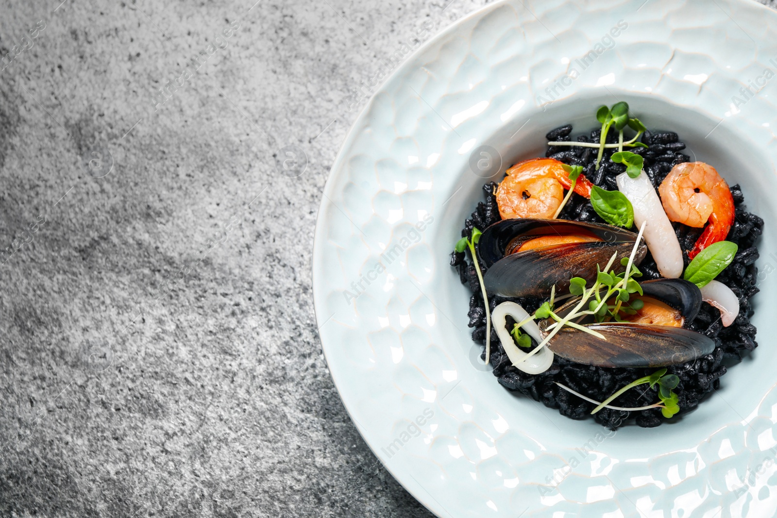 Photo of Delicious black risotto with seafood on grey table, top view