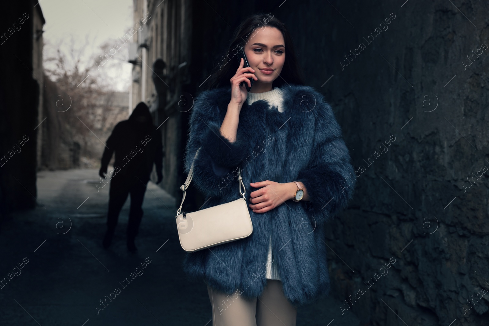 Photo of Man stalking young woman while she talking on phone in alley