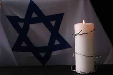 Photo of Flag of Israel, Barbed wire and burning candle on black background. Holocaust memory day