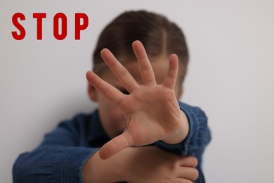 Image of No child abuse. Girl making stop gesture near white wall, selective focus