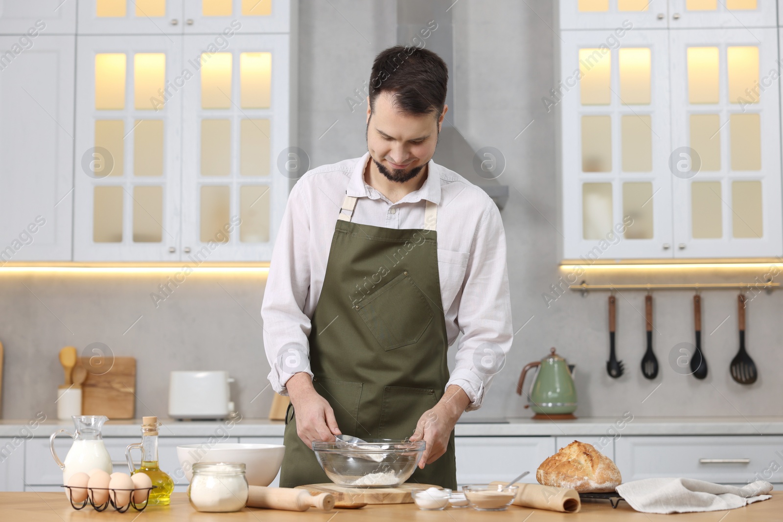 Photo of Making bread. Man putting flour into bowl at wooden table in kitchen