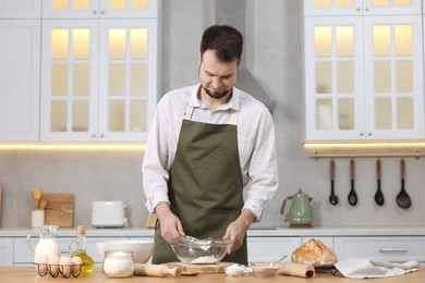 Making bread. Man putting flour into bowl at wooden table in kitchen