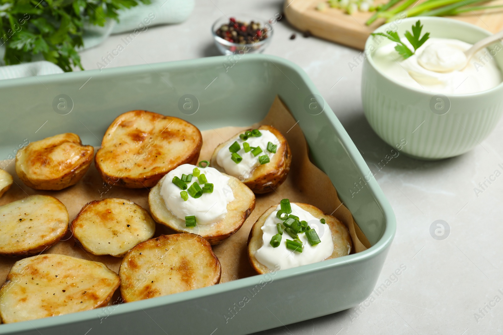 Photo of Sour cream and delicious potato wedges on light grey table