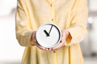 Photo of Young woman holding alarm clock on blurred background. Time concept