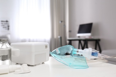 Photo of Modern nebulizer with face mask and medicines on white table indoors. Equipment for inhalation