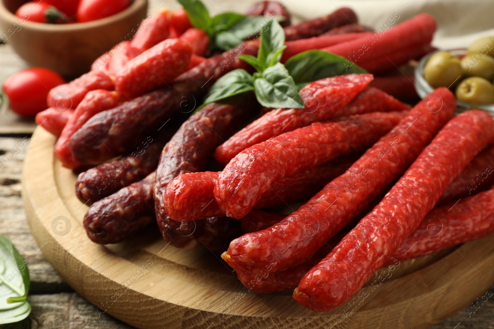 Photo of Different thin dry smoked sausages and basil on wooden table, closeup