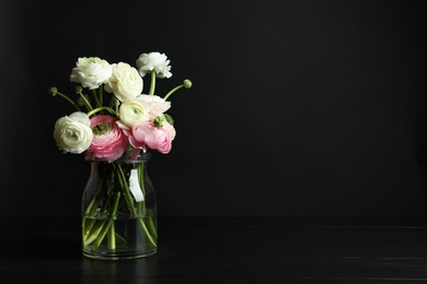 Photo of Glass vase with beautiful ranunculus flowers on black background