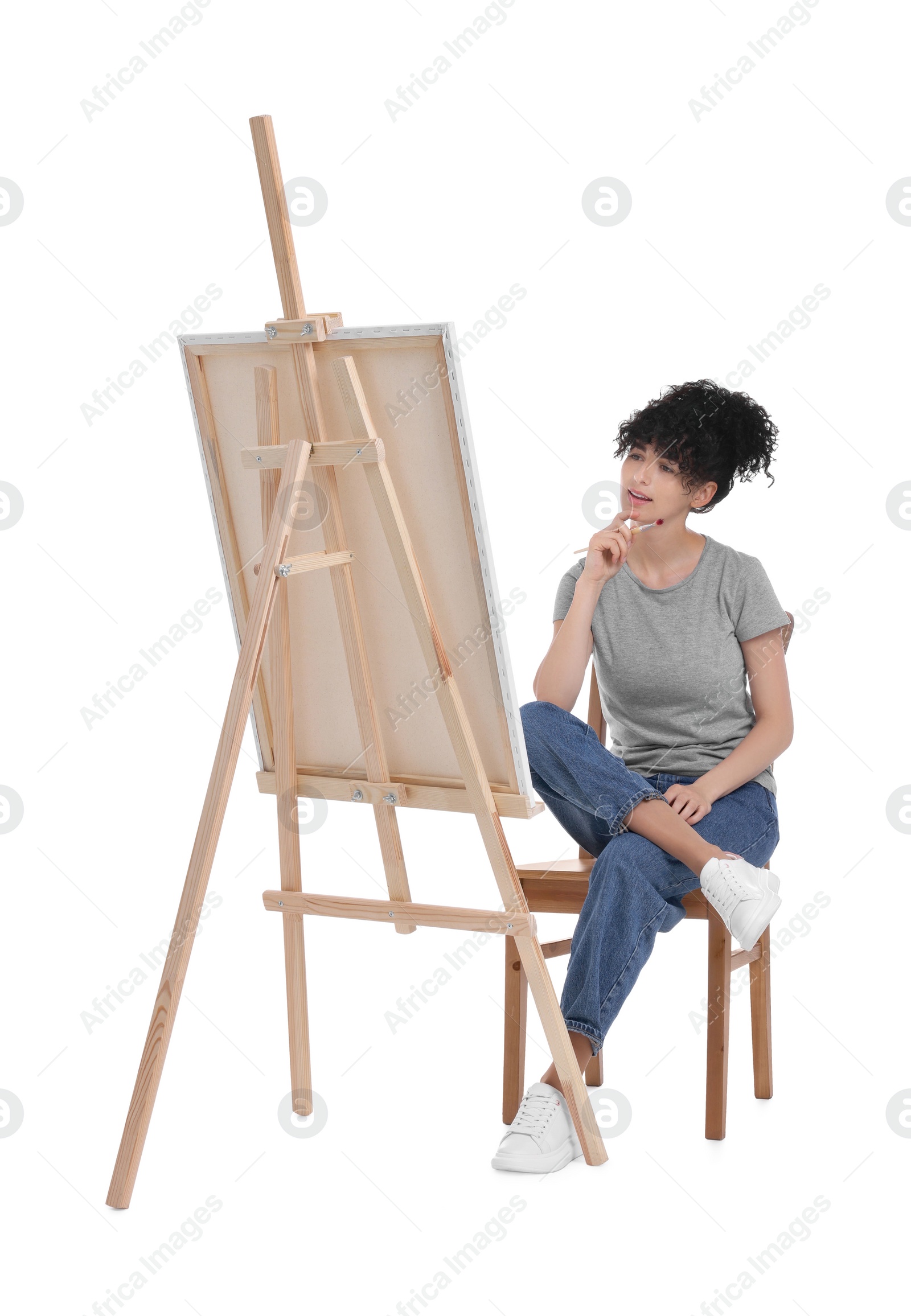 Photo of Young woman holding brush near easel with canvas against white background