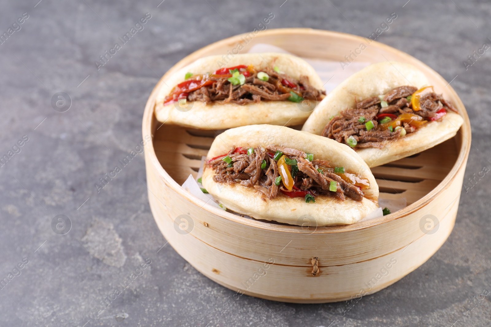 Photo of Delicious gua bao in bamboo steamer on grey table. Space for text