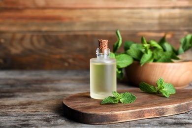 Essential oil in glass bottle and mint on wooden table. Space for text