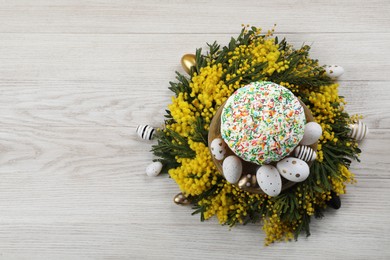 Photo of Traditional Easter cake with sprinkles, painted eggs and beautiful spring flowers on white wooden table, top view. Space for text