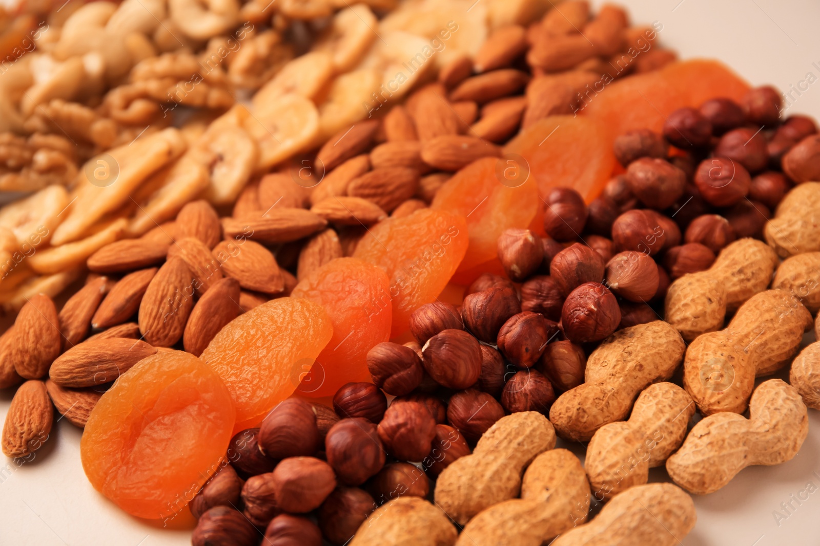 Photo of Mix of delicious dried nuts and apricots on beige background, closeup