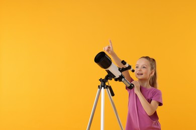 Photo of Excited little girl with telescope pointing at something on orange background, space for text