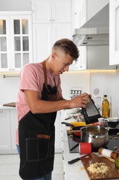 Photo of Man grating cheese into saucepan in messy kitchen. Many dirty dishware and utensils on stove and countertop