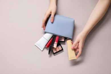 Photo of Woman with cosmetic bag and different makeup products on beige background, top view