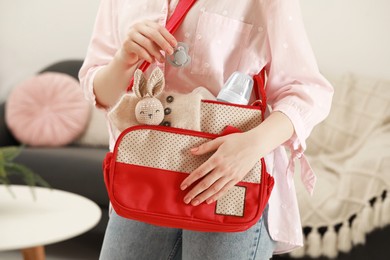 Photo of Woman putting pacifier into mother`s bag indoors, closeup