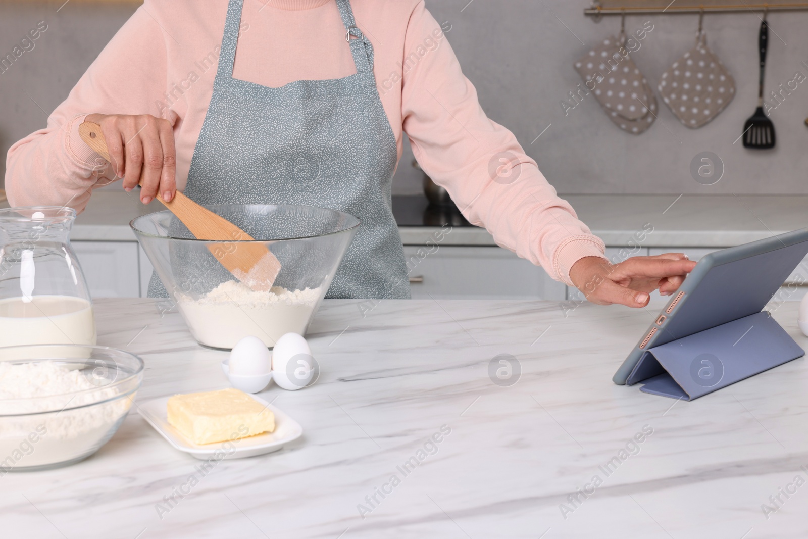 Photo of Woman reading recipe on tablet while cooking in kitchen, closeup. Online culinary book