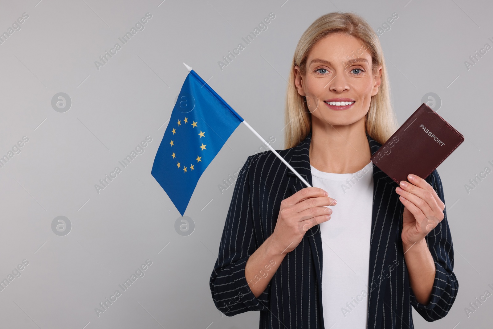 Photo of Immigration. Happy woman with passport and flag of European Union on gray background, space for text