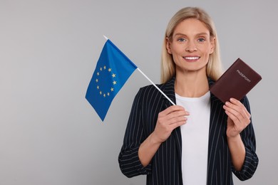 Immigration. Happy woman with passport and flag of European Union on gray background, space for text