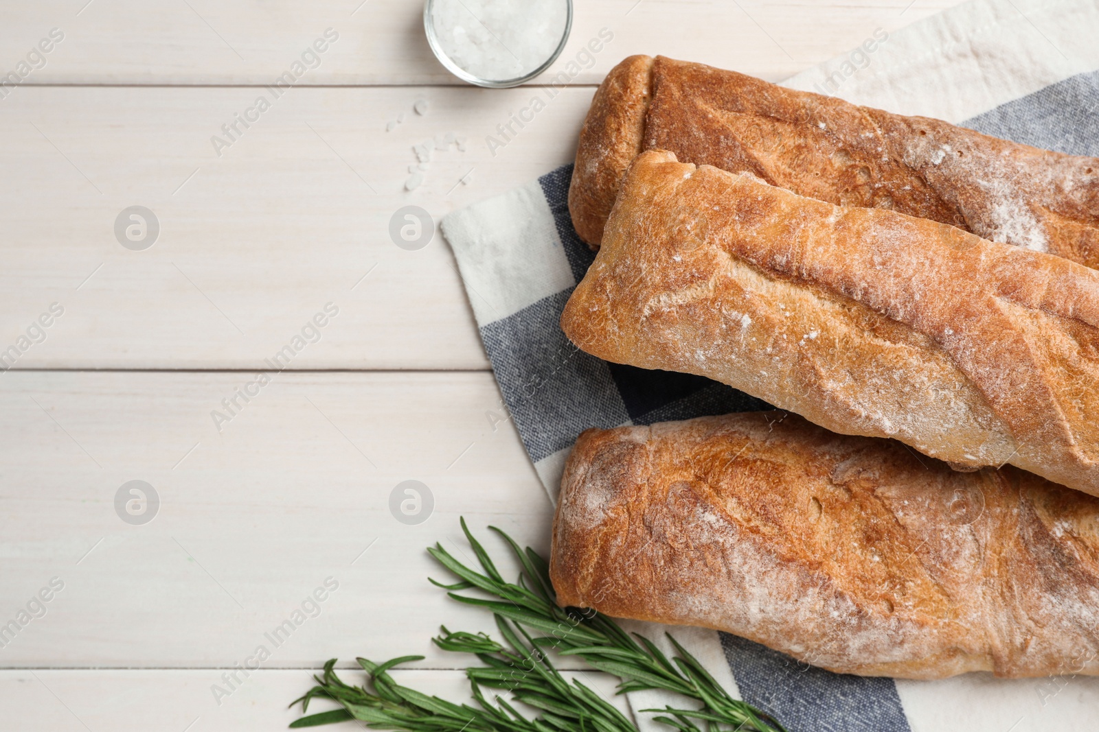 Photo of Delicious French baguettes and rosemary on beige wooden table, flat lay. Space for text