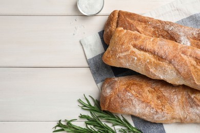 Photo of Delicious French baguettes and rosemary on beige wooden table, flat lay. Space for text