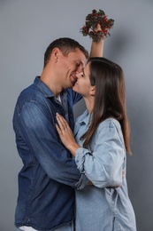 Happy couple kissing under mistletoe wreath on grey background