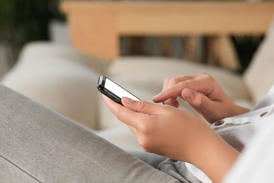 Photo of Woman using smartphone on sofa at home, closeup
