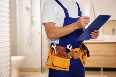 Plumber with clipboard and tool belt in bathroom, closeup. Space for text
