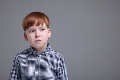 Portrait of sad little boy on grey background, space for text